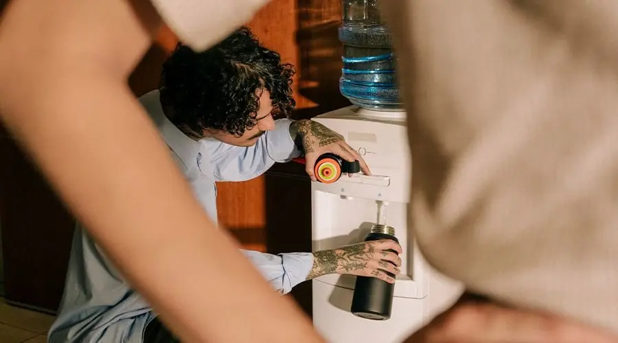 A man fills up his steel air up bottle at an office water cooler